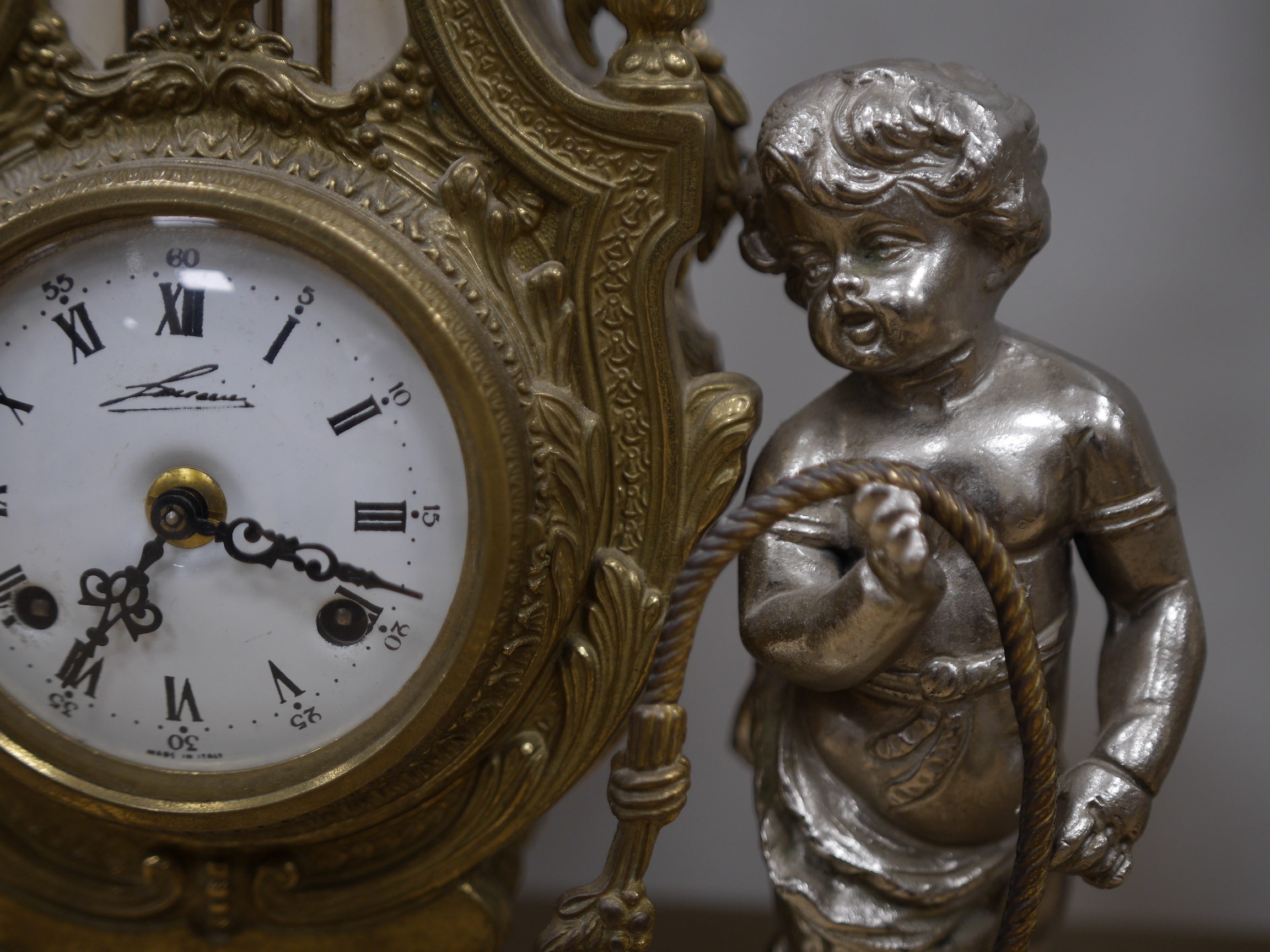 An ornate mixed metal putti clock and five light garniture, garnitures 59.5cm high. Condition - fair to good